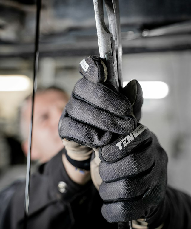 The image shows a close-up of a mechanic's gloved hands working on a vehicle.